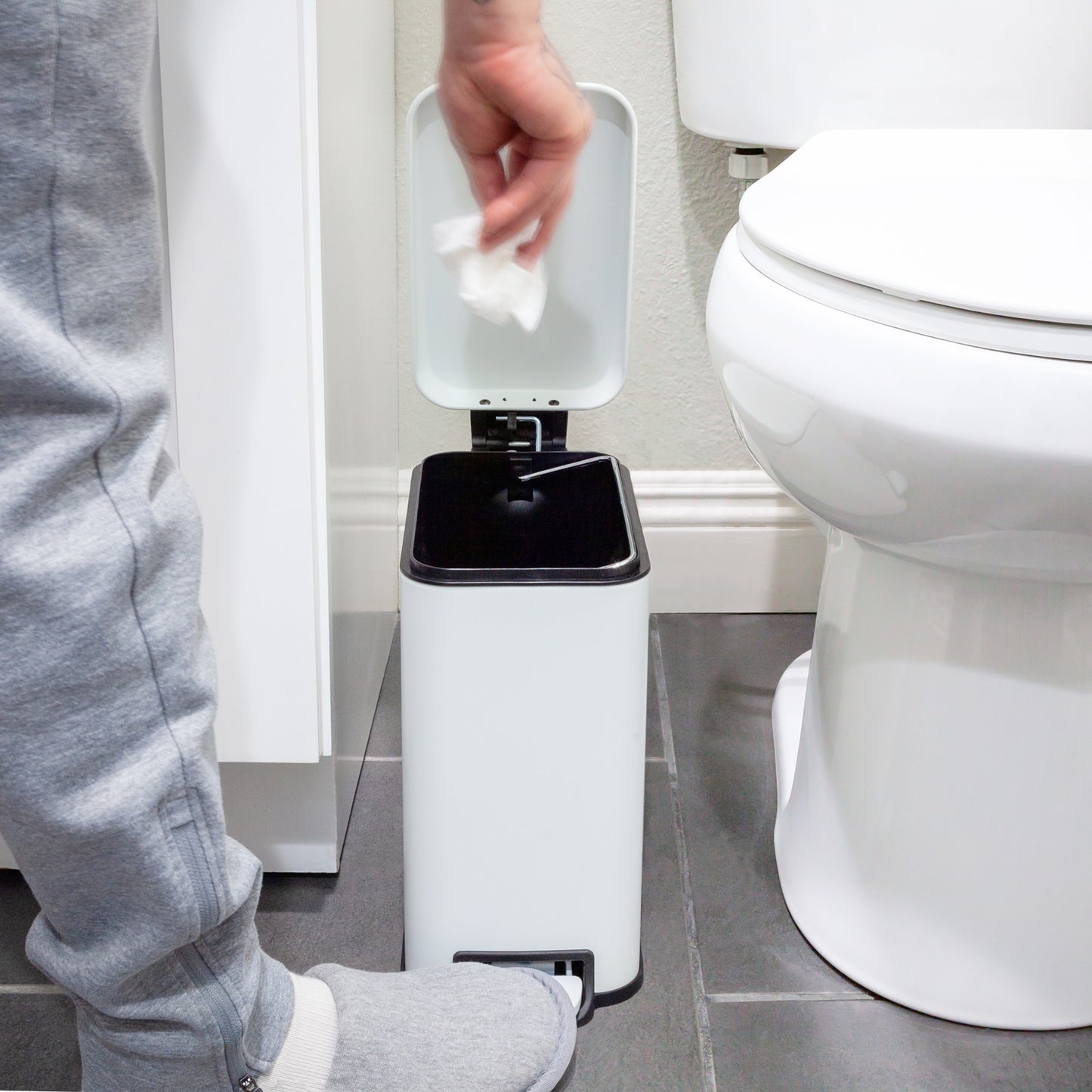 Slim white step trash can fitting beside a bathroom toilet