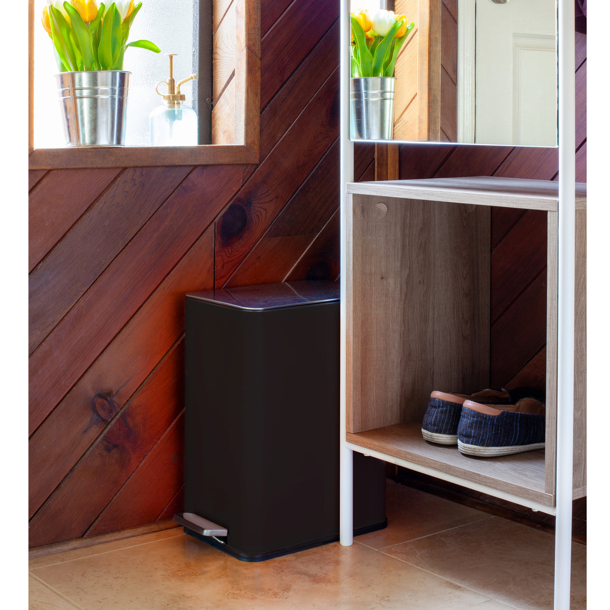 Slim black step trash can fitting beside furniture in a compact space