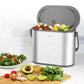 Small stainless steel countertop compost bin filled with kitchen food scraps