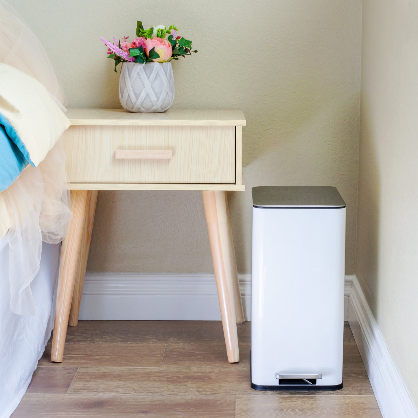 White slim trash can beside nightstand in a small bedroom